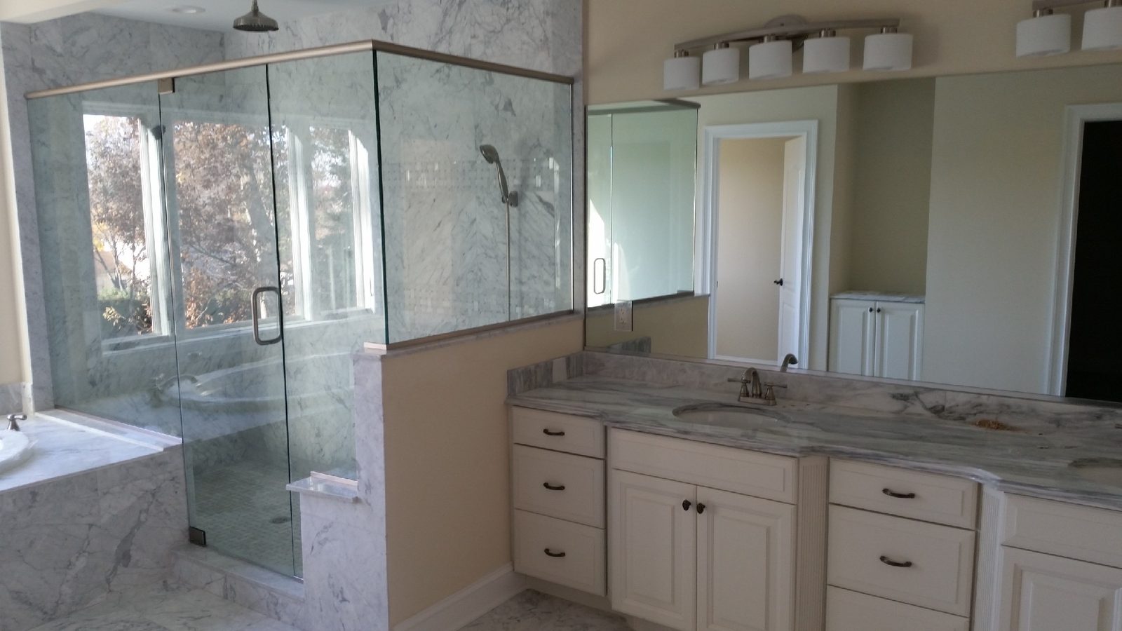 Residential bathroom with frameless vanity mirror and glass shower enclosure installed by Illusions